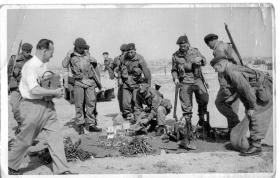 Paratroopers crowd around piles of arms and ammunition on the ground. 
