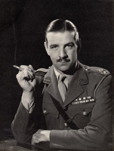 Black and white image of Lt Col Lonsdale leaning on a table smoking a cigarette