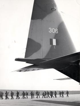 AA Tail fin of an RAF C130K with paratroopers walking below