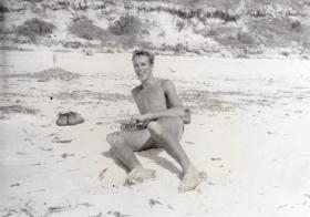 A shirtless Pte Green relaxing on a beach.