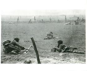 American troops equipped with an M1919 A6 inch along flat ground toward their objective.