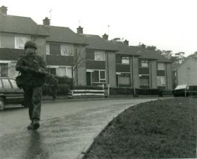 Paratrooper holding a SA 80 gun on foot patrol through a housing estate.