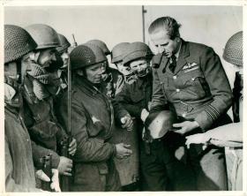 Airborne soldiers crowd round a German helmet taken as a souvenir.