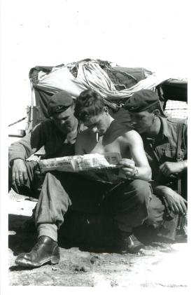 Three paratroopers crouch and read a paper in the Canal Zone.
