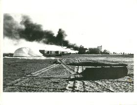 Buildings burn on El Gamil airfield. A recently dropped container can also be seen.