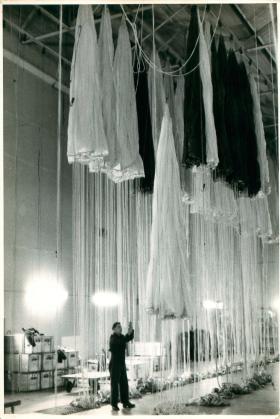 Several white parachutes in the drying hangar at Ringway.