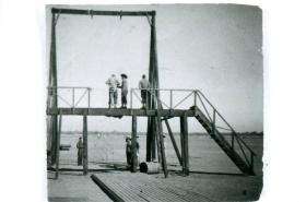 Men standing on wooden swing harness used for teaching parachute control.