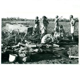 Men from 1st Airlanding Light Regiment RA spread their ammunition on the ground and     discuss the opening range.