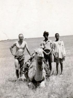 Gunner Poole of the 211 Airlanding Light Battery RA with locals and camel, Rafa, Palestine, 7 September 1946.
