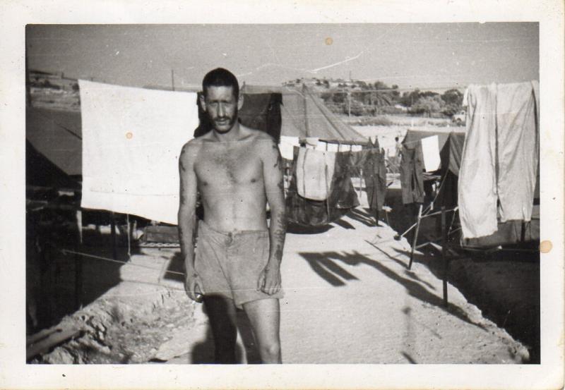 Joe lee wearing just his shorts standing near washing drying on a line hanging between tents.