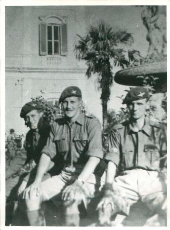 Three officers from A Company 3rd Parachute Battalion sit on a wall in a courtyard.