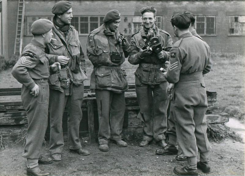 Three war correspondents in uniform and with cameras talk to their colleagues.