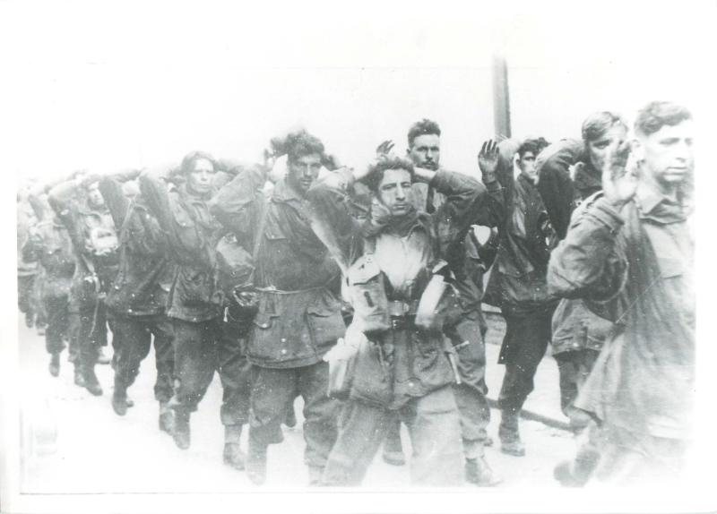 Captured British paratroopers march to captivity with their hands on their heads.