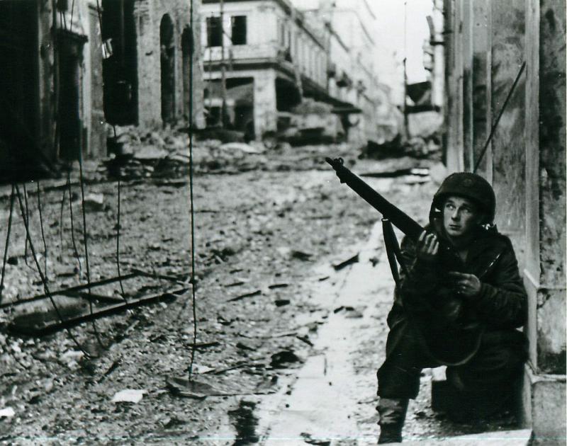 A soldier crouches with his gun in a street destroyed by fighting.