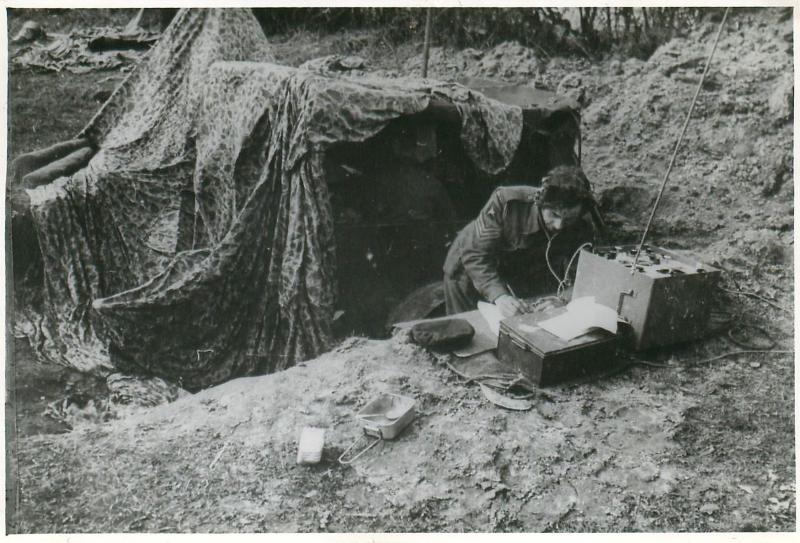 Airborne signaller at his post under a camoflaged parachute.