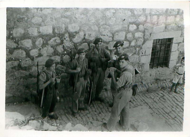 Five paratroopers have a tea break on a cobbled street in Palestine.