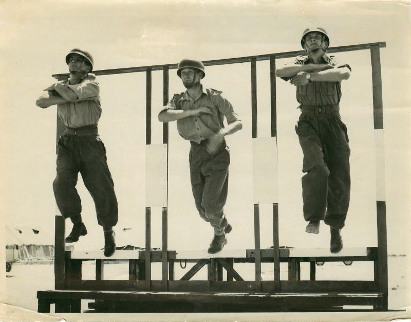 Three men jump a wooden structure for aircraft exit training.