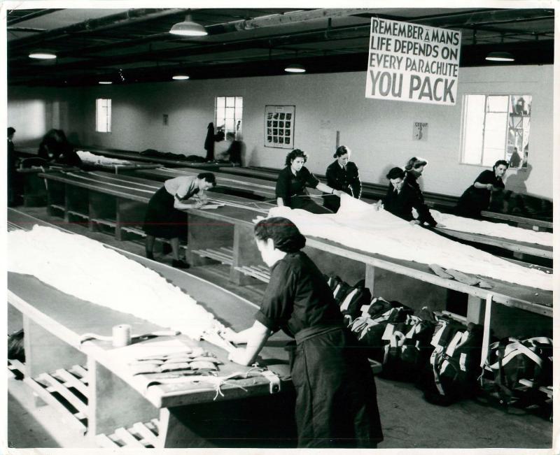 Women packing parachutes on long tables.