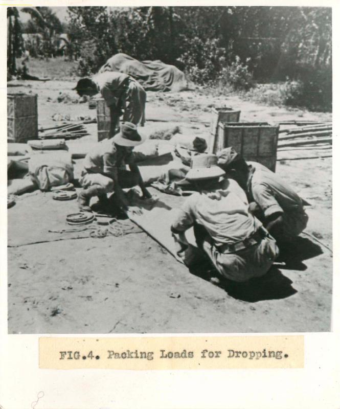 Men from No.1 Indian Air Company squat on teh floor outdoors and pack loads for dropping.