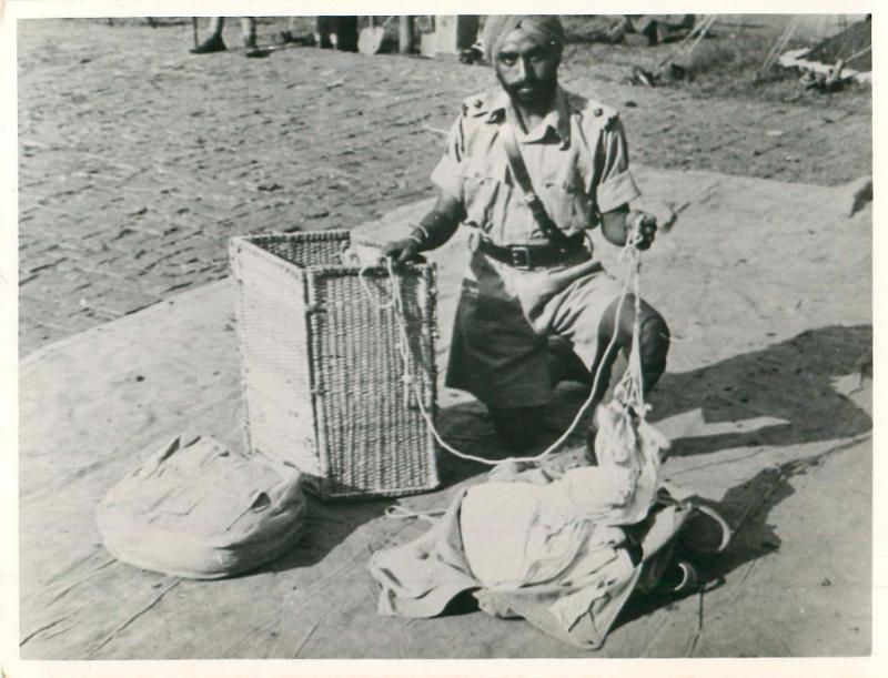 Sikh airborne officer kneels on the ground and packs loads for dropping.
