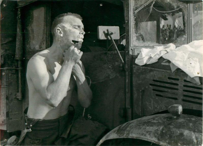 Sergeant Huntly using the mirror of a military vehicle to shave.