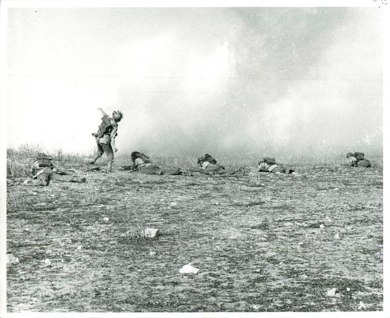 Paratrooper throws a grenade while others take cover on the ground. July, 1943.