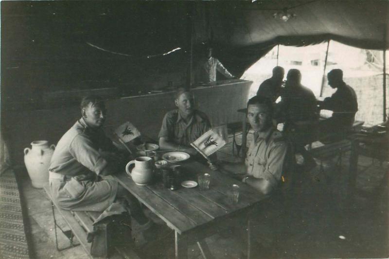 Six men of 1st Airlanding Brigade sit round tables after a meal in their makeshift mess. 