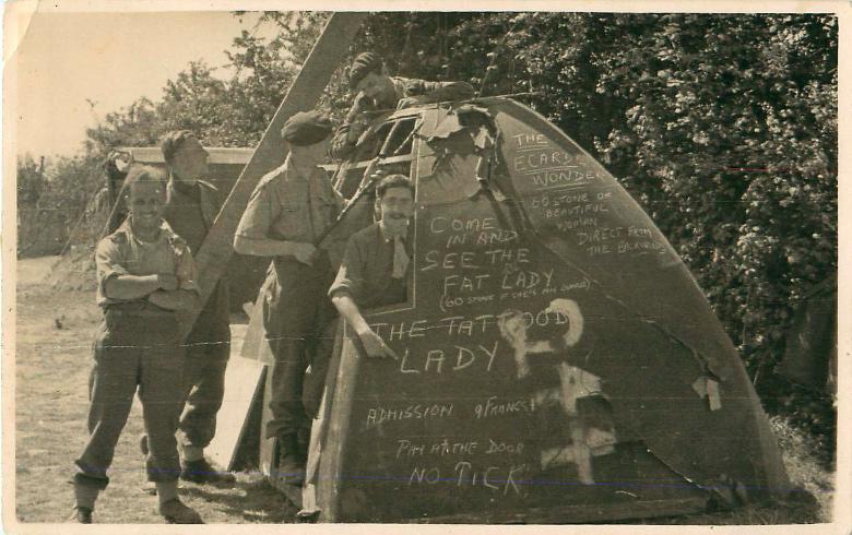 Five airborne soldiers stand beside humorous graffiti in Normandy.